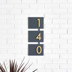 a white brick wall with a black and gold house number sign next to a potted plant