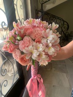 a bouquet of pink flowers in a vase on a table with a woman's hand holding it