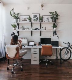 a woman sitting at a desk in front of a wall with plants and pictures on it