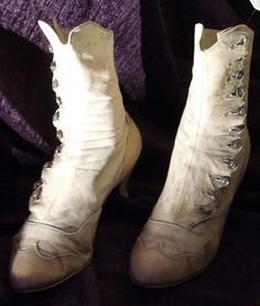 a pair of white boots sitting on top of a purple bed cover next to a pillow