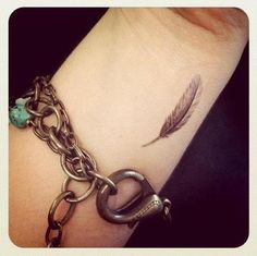 a wrist tattoo with a feather on it and a chain attached to the wrist that says love that it's so small but detailed