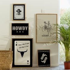 several framed pictures hang on the wall next to a potted plant and a wicker basket