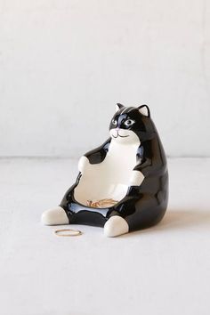 a black and white cat figurine sitting on the ground with its paw in it's mouth