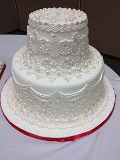 a three tiered white wedding cake with red ribbon on the table next to it