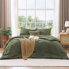 a bed with green sheets and pillows in front of a window