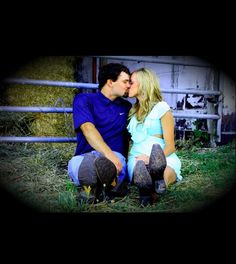 a man and woman sitting next to each other in front of a fence with hay