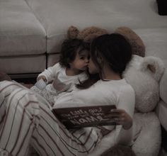 a woman and child are sitting on the floor reading a book with teddy bears behind them