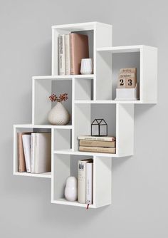 a white shelf with books and vases on it's sides, against a gray wall