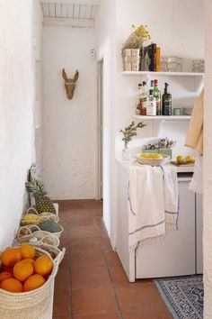 a white kitchen with oranges and bottles on the counter next to a basket full of fruit