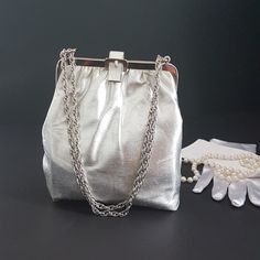 Silver shimmery cloth clutch purse with adjustable, silver tone metal chain strap.  Use a double chain and hang from the wrist or slide the chain and hang from the shoulder (would sit about the upper arm)  Belt shaped clasp lock at the top. Silver-tone metal frame. Lined with muted mauve-taupe  sateen.   Hang from the wrist or fingertips or convert to a clutch. Room for makeup essentials, as seen in pictures, with room to spare for a small cell phone Tag:  Ink Stamp on inside lining but unable t Arm Belt, Wrist Purse, Mauve Taupe, Double Chain, Ink Stamps, Canada Post, Makeup Essentials, Clutch Purse, Clutch Handbag