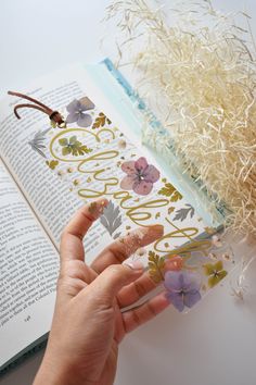 a person is holding an open book with flowers on it and the pages are covered in gold foil