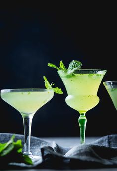 three glasses filled with green drinks on top of a table next to some mint leaves