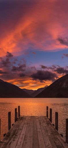 a wooden dock sitting on top of a lake under a colorful sky