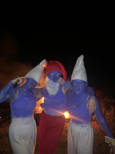 three people with blue paint on their faces and body are standing in front of a fire