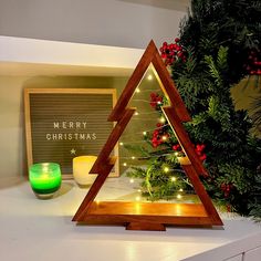 a wooden triangle with christmas lights on it sitting on a counter next to a candle