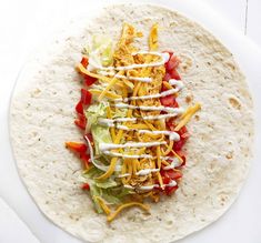 a tortilla topped with chicken, lettuce and tomatoes on a white plate