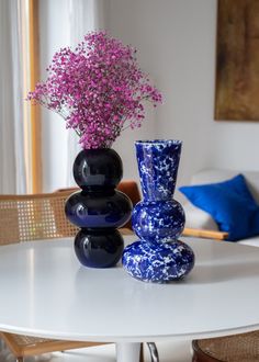 two vases with purple flowers sit on a white table in front of a couch