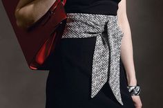 a woman in a black and white dress is holding a red purse with her right hand