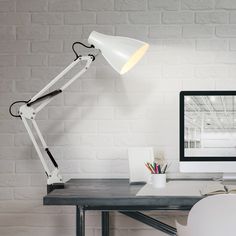 a white desk lamp sitting on top of a wooden desk next to a computer monitor