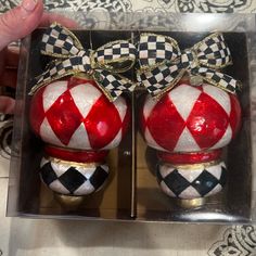 two red and white christmas ornaments in a box with bows on the top one has a black and white checkerboard pattern