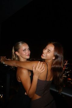 two beautiful young women standing next to each other in front of a city at night