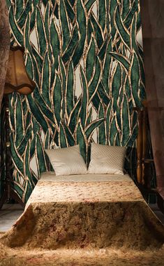 a bed sitting in front of a green wallpaper with leaves and branches on it