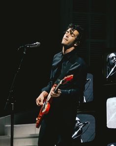 a man standing in front of a microphone and holding an electric guitar with his right hand