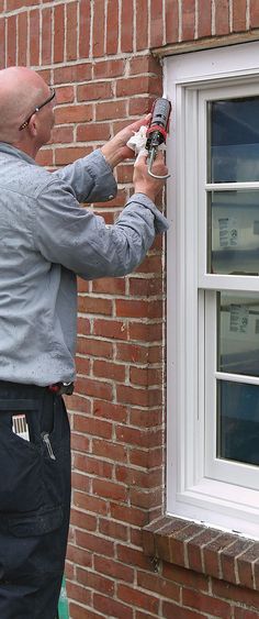 a man working on a window with a drill and screwdriver in front of a brick building