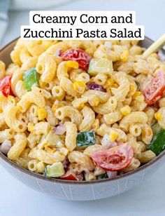 a bowl filled with macaroni salad on top of a white table next to a gold spoon