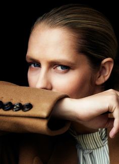 a woman with blue eyes is hiding her face behind a brown coat and buttoned shirt