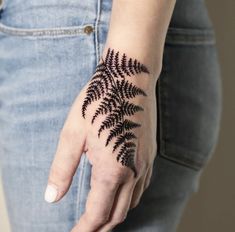 a woman's hand with a black fern tattoo on it