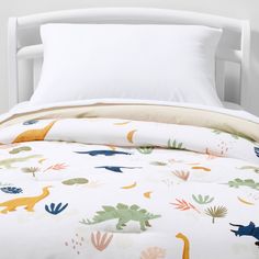 a bed with white sheets and dinosaur print on it, along with two pillow cases