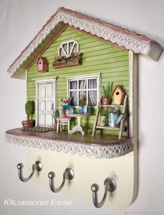 there is a green house on the wall with two hooks in front of it that are holding potted plants