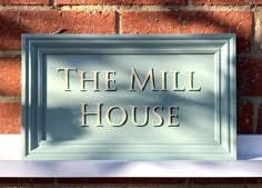 a sign that reads the mill house on it's front door and is next to a brick wall