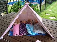 three dolls are laying in a teepee tent on a picnic table with blue and pink pillows