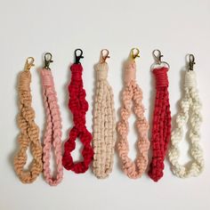 five different colored macrame bracelets hanging from hooks on a white wall,