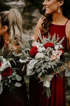 two bridesmaids in red dresses hold bouquets of flowers and greenery as they look at each other