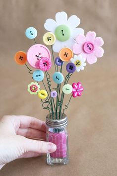 a hand holding a jar filled with buttons and flowers