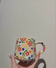 a hand holding a colorful coffee cup in front of a white wall with flowers on it