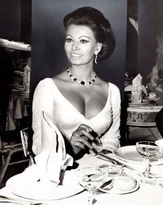 a woman sitting at a table in front of a wine glass and plate with utensils on it