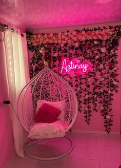 a pink room with a hanging chair and flowers on the wall, along with a neon sign