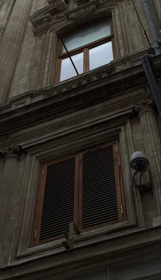 an old building with shutters and a clock on the front window is seen from below