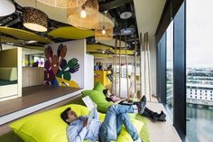 two men are lounging on bean bags in an office lobby with large windows and colorful artwork