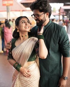 a man standing next to a woman in a green and white sari on the street