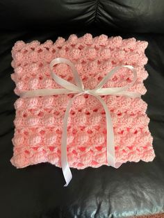 a pink crocheted blanket with a white bow on it sitting on a black leather couch