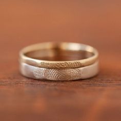 two wedding bands with fingerprints on them sitting on top of a wooden table