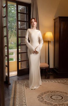 a woman standing in front of a doorway wearing a white dress and posing for the camera