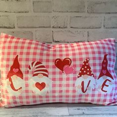 a red and white gingham pillow with gnomes on it, sitting in front of a brick wall