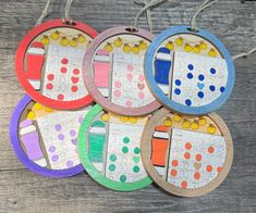 four different colored wooden circles with numbers and shapes on them, hanging from strings in front of a wood table