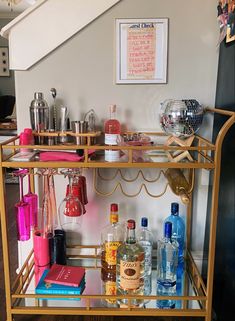 a bar cart with liquor bottles and glasses on the top shelf next to a stair case